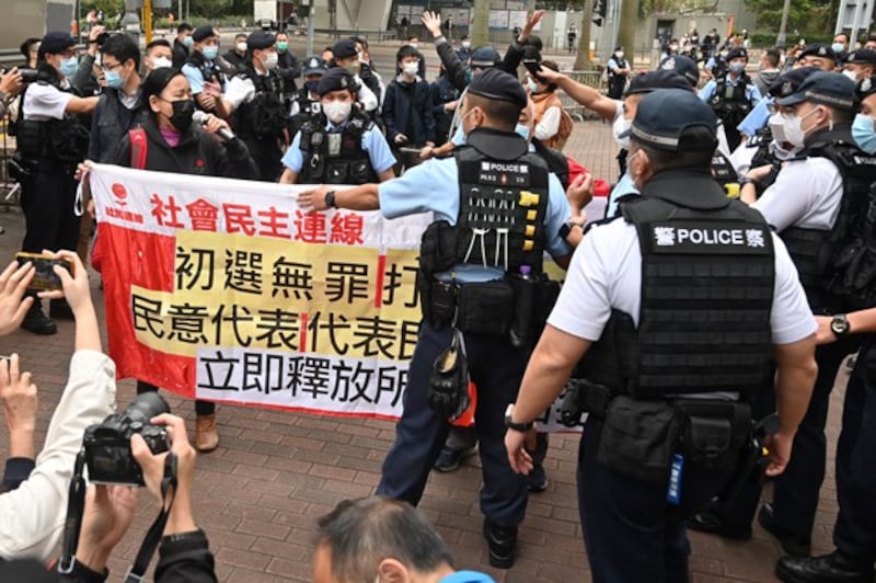 Members of the League of Social Democrats are surrounded by police as they carry a banner outside a court in Hong Kong on February 6, 2023, as the trial of 47 of Hong Kong's most prominent pro-democracy figures begins in the largest prosecution under a national security law that has crushed dissent in the city. Credit: AFP
