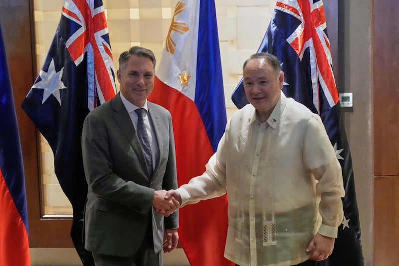 Two men shaking hands with the Australian and Philippine flags behind them.